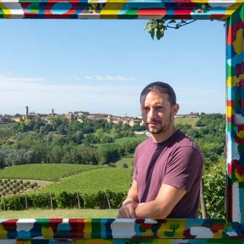 a man standing inside a very colorful frame with the Bosco vineyards in the background