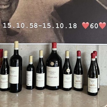 Bottles of Rubinelli Vajol wine lined up on a table under a poster of a photo from 1958 celebrating 60 years